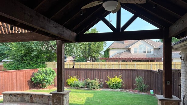 A covered patio area with stone flooring, a wooden ceiling, and a view of a backyard with a wooden fence and greenery. - Backyard Sanctuary with 4 Bedrooms House (Plano)
