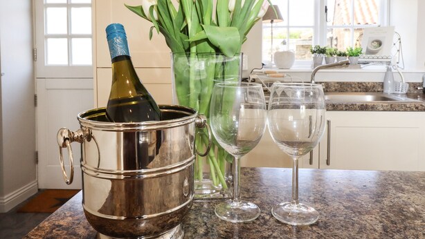 Una cocina con una botella de vino en un cubo metálico, dos copas de vino y un jarrón con tulipanes.