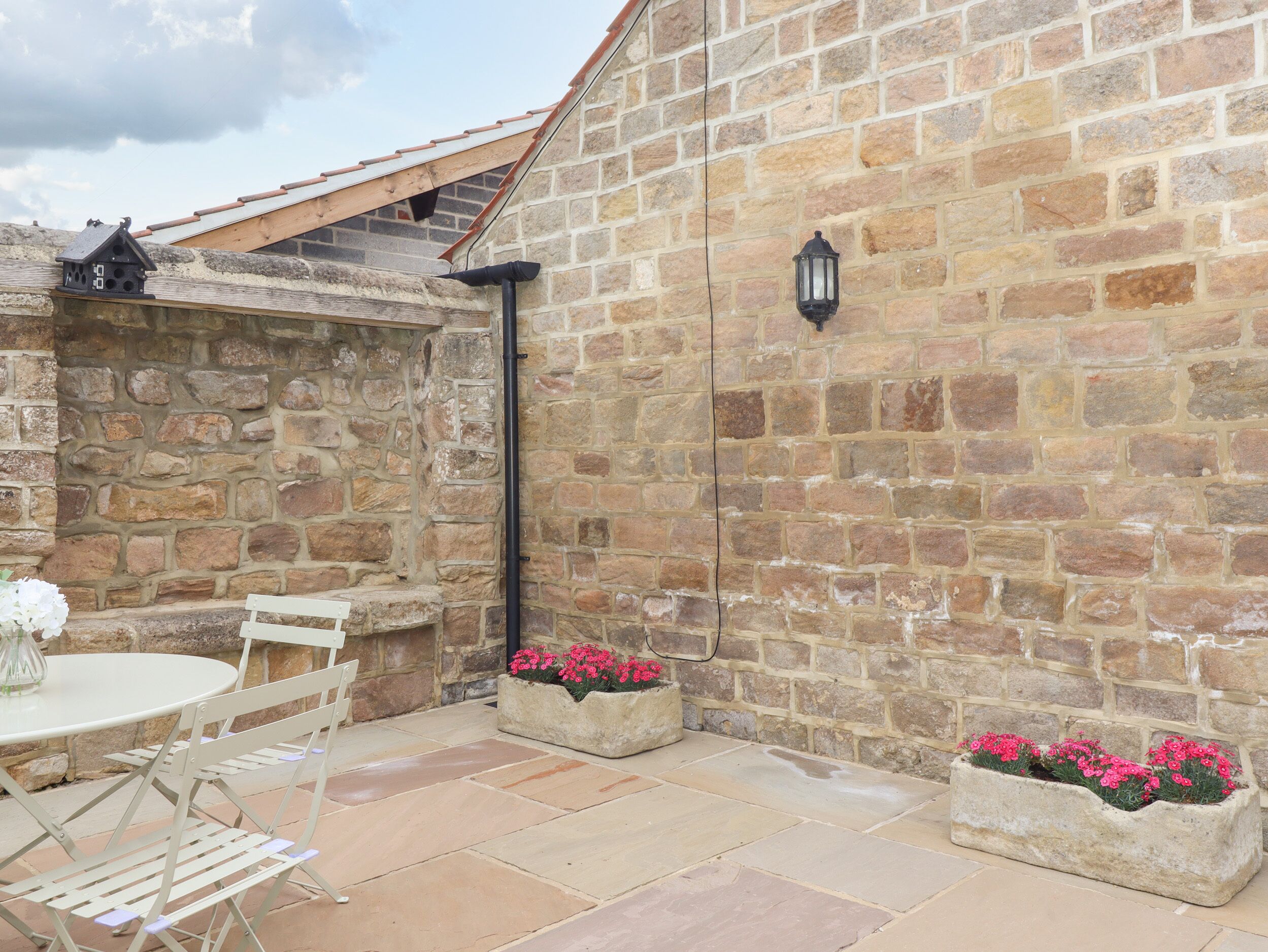 A stone building with a tiled patio, a round table with chairs, and flower planters.