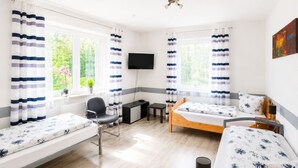 Ein Zimmer mit zwei Betten, einem Schreibtisch, einem Stuhl, einem Fernseher und einem Fenster mit Vorhängen.
