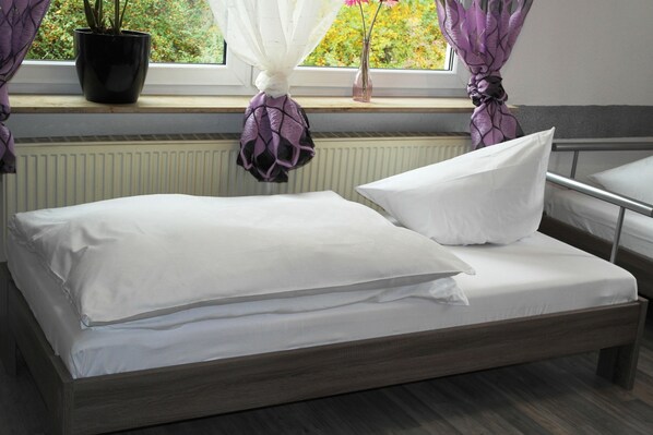 A bed with white bedding, a window with curtains, a potted plant, and a radiator.