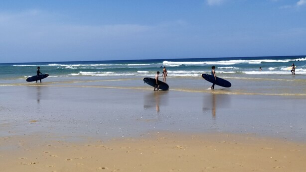 Ein Strand mit Menschen, die spazieren gehen und Surfbretter tragen.