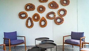 Une pièce comprenant deux chaises en bois avec des coussins violets, une petite table ronde et un mur décoré d’œuvres d’art circulaires en bois.