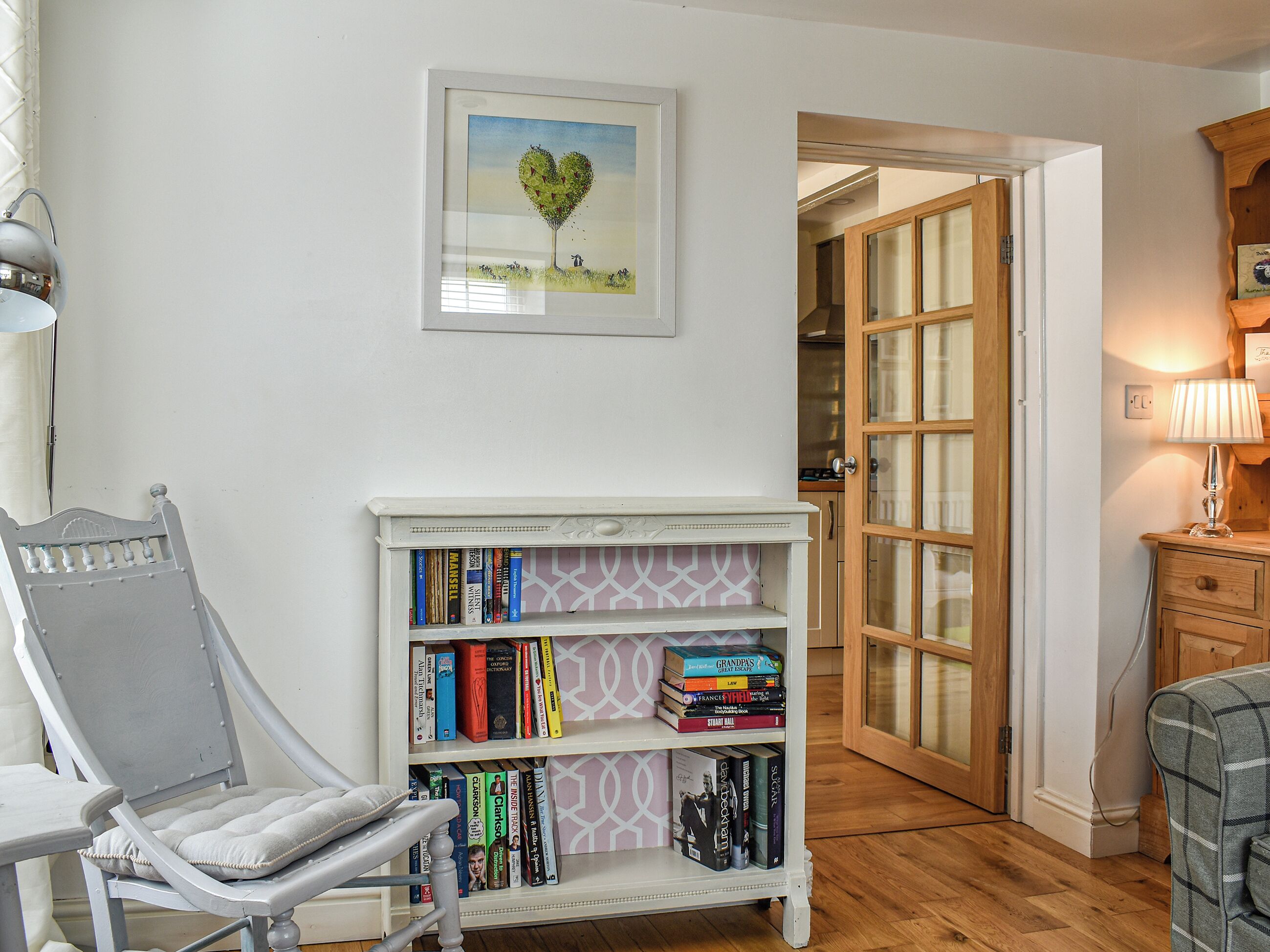 Una habitación con una estantería, una silla y una puerta que da a otra estancia.