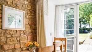 Un banc en bois avec un vase de fleurs, un tableau encadré accroché à un mur de pierre et une porte vitrée donnant sur l’extérieur.
