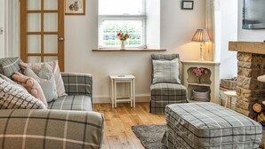 Un salon chaleureux avec un canapé à carreaux, une petite table d’appoint, une lampe et une cheminée.
