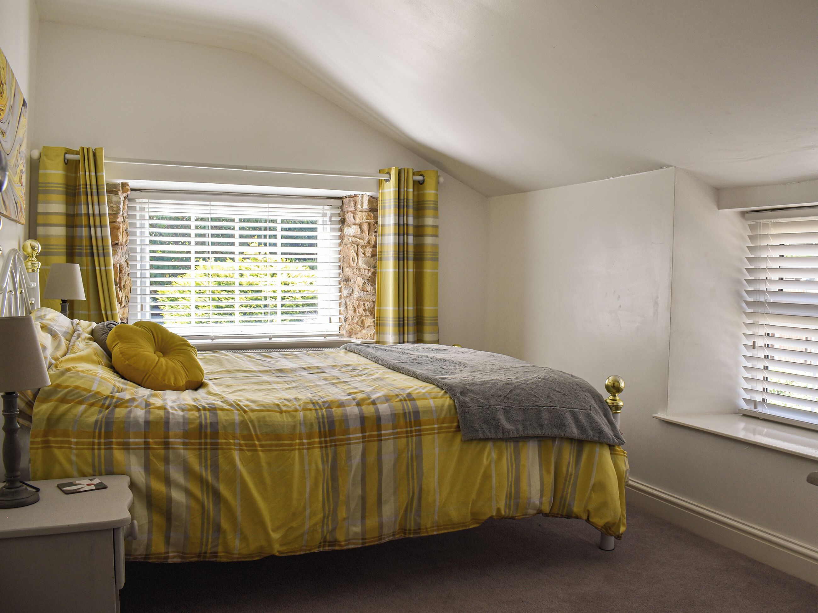 A bedroom with a bed, a nightstand, a lamp, and a window with blinds.
