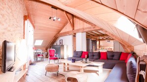 Un loft spacieux avec de hauts plafonds, des poutres apparentes, un ensemble de canapés, un coin repas et un téléviseur.