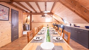 Un intérieur en bois avec une table à manger dressée pour six personnes, une cuisine en arrière-plan et un plafond en pente.