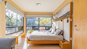 Une chambre moderne avec un grand lit, un banc et une vue sur la ville grâce à de grandes fenêtres.