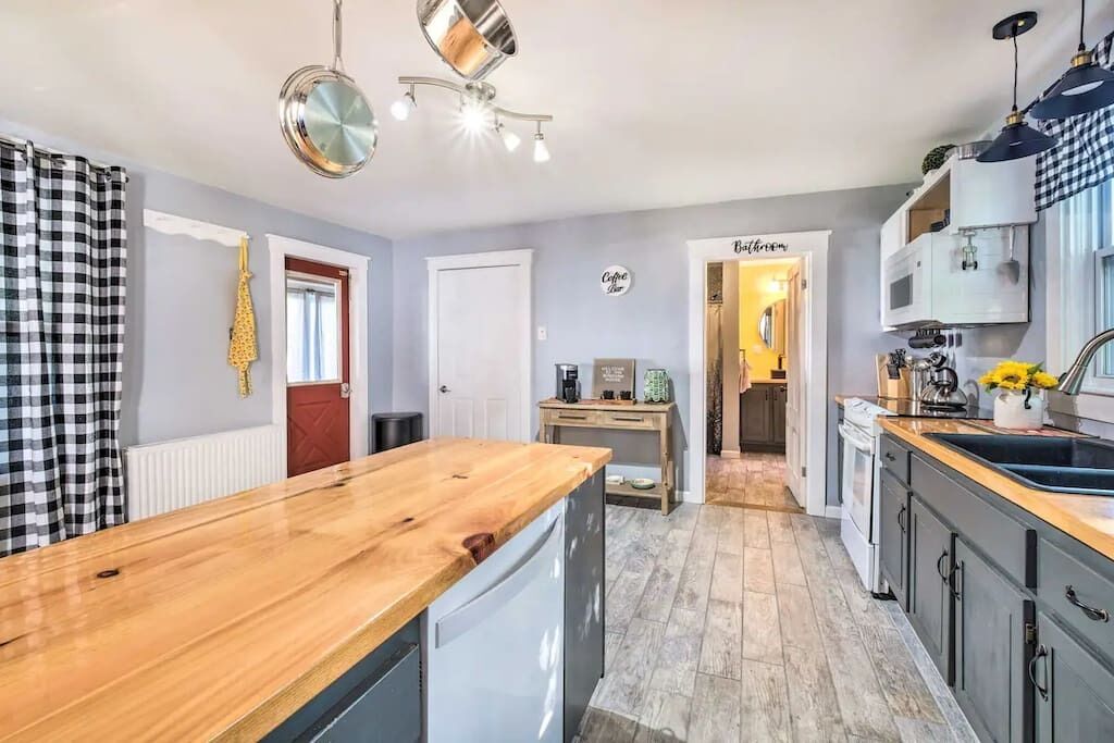 Una cocina moderna con encimera de madera, lavavajillas integrado y un lavabo. Hay una cafetera y un hervidor en la encimera.