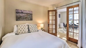 Ein Hotelzimmer mit einem Bett, einem Bild an der Wand, einer Tür zu einem Balkon und einem Stuhl davor.