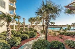 A resort with a pool, palm trees, and a pathway leading to a building.