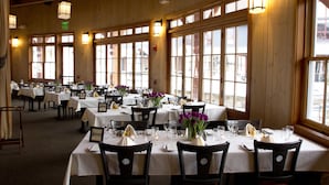 Un restaurant doté de nombreuses tables dressées pour le service, de grandes fenêtres et de luminaires suspendus.