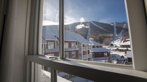 Une vue depuis une fenêtre donnant sur une ville enneigée, avec des bâtiments et une montagne en arrière-plan.