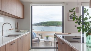 A modern kitchen with wooden cabinets, a white countertop, and a view of the beach through a glass door.
