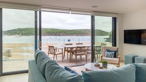 A modern living room with a large sliding glass door leading to a balcony overlooking a beach.