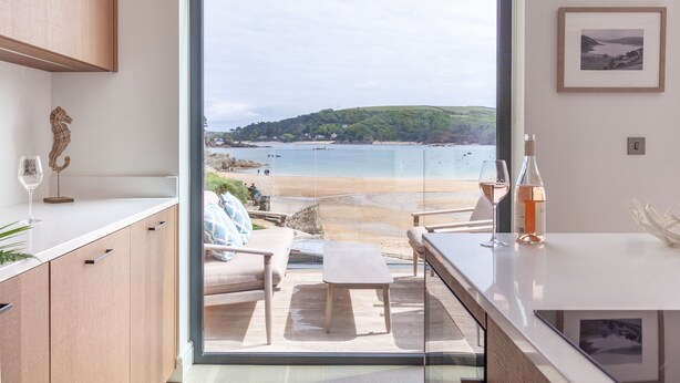 A modern kitchen with a large sliding glass door leading to a balcony overlooking a beach.