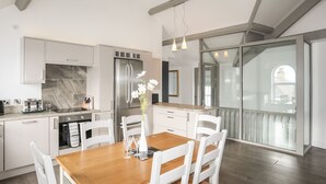 Una cocina moderna con armarios blancos, un refrigerador de acero inoxidable y una mesa de comedor de madera con sillas blancas.