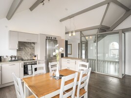 Una cocina moderna con armarios blancos, un refrigerador de acero inoxidable y una mesa de comedor de madera con sillas blancas.