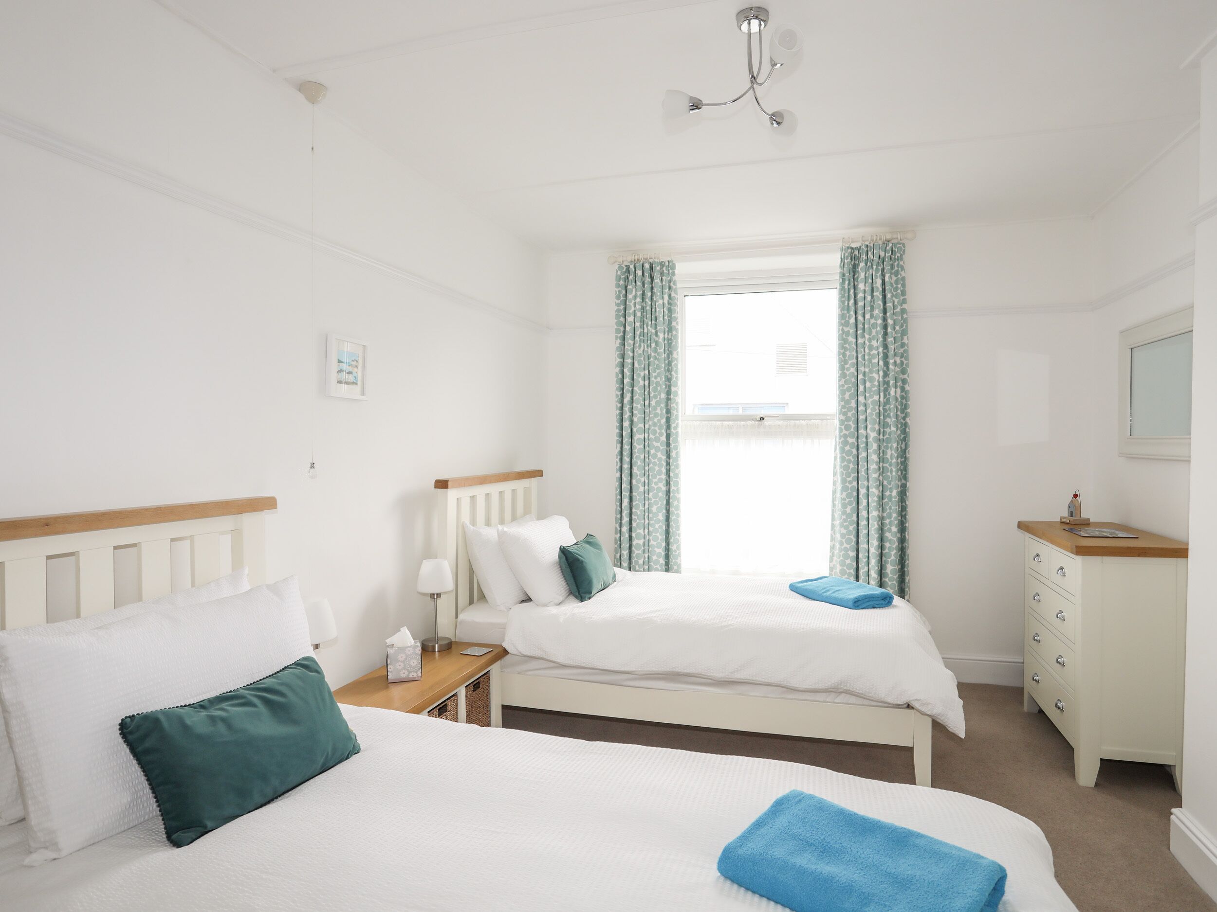 A hotel room with two single beds, a wooden nightstand, a dresser, and a window with curtains.