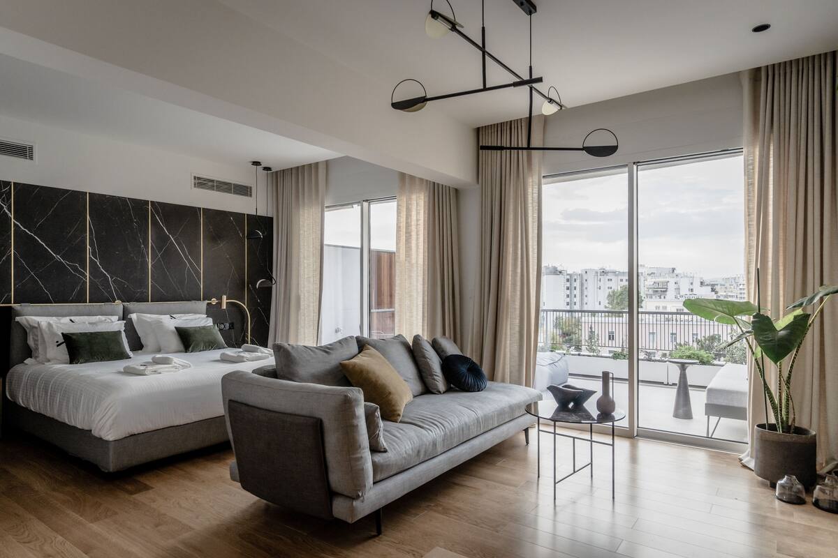Una habitación de hotel moderna con una cama grande, un sofá y un balcón con vista a la ciudad.