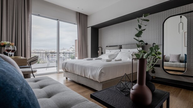 A modern bedroom with a large bed, a view of the city, and a balcony. - Athinaion Recreation Suites (Athens)