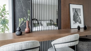 A modern room with a wooden desk, two grey upholstered chairs, a black and white photograph, and a plant. - Athinaion Recreation Suites (Athens)
