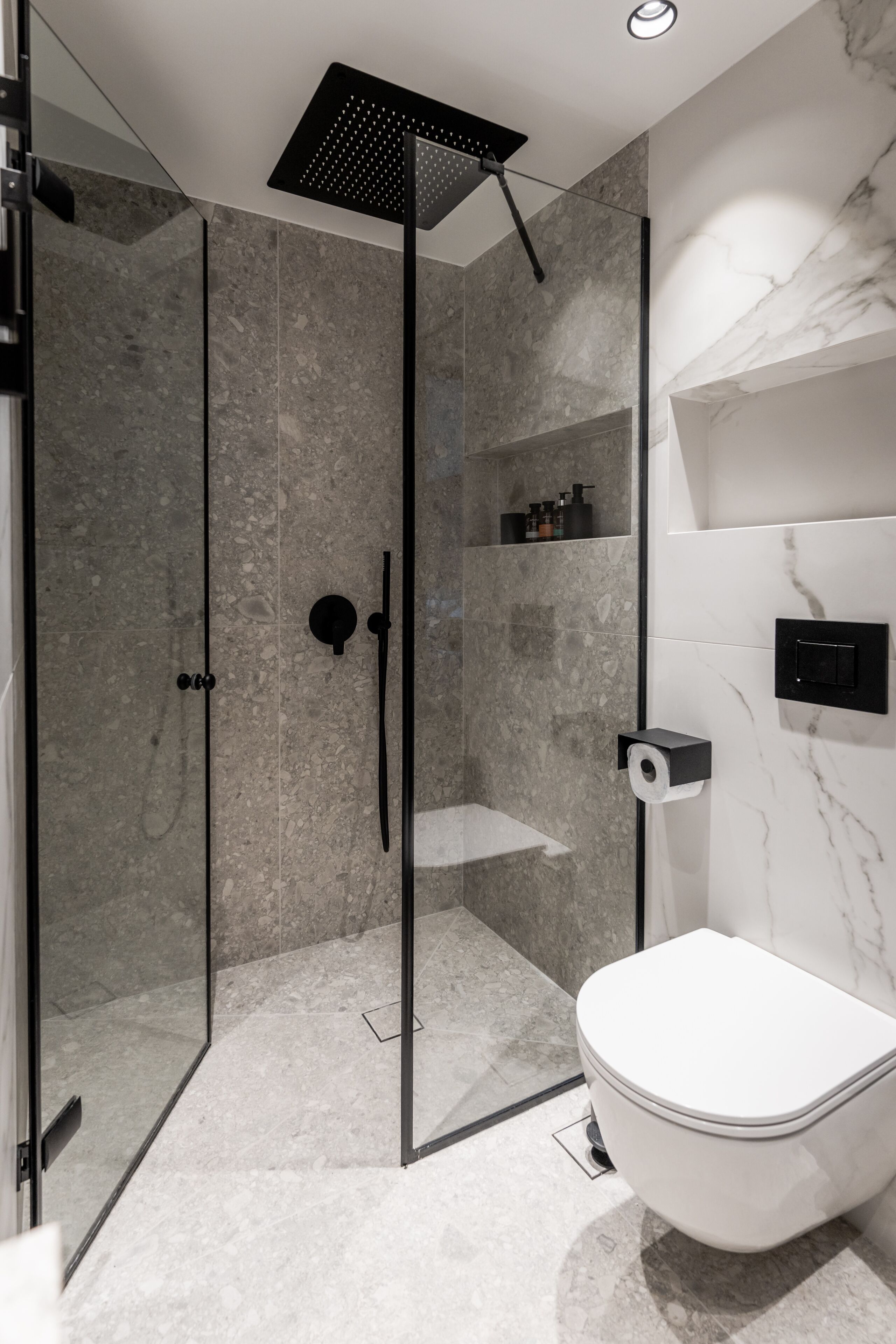 A modern bathroom with a glass-enclosed shower, a toilet, and marble walls.