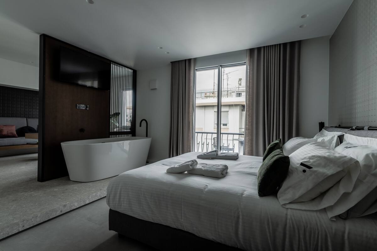 Una habitación de hotel moderna con una cama grande, una bañera integrada y vistas a la ciudad.