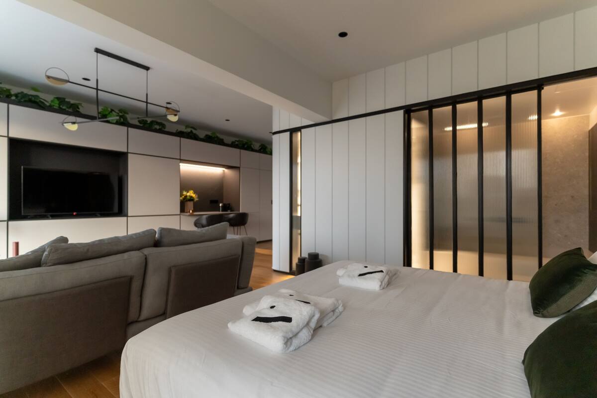Una habitación de hotel moderna con una cama grande, un sofá, un televisor de pantalla plana y un balcón al que se accede por una puerta corrediza.