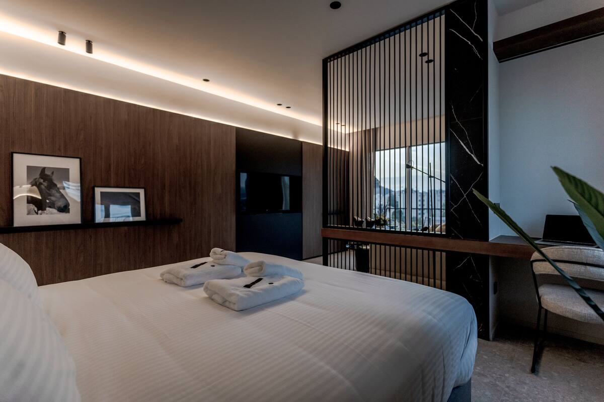 Una habitación de hotel moderna con una cama grande, un panel de madera decorativo, una ventana con marco negro y una planta.