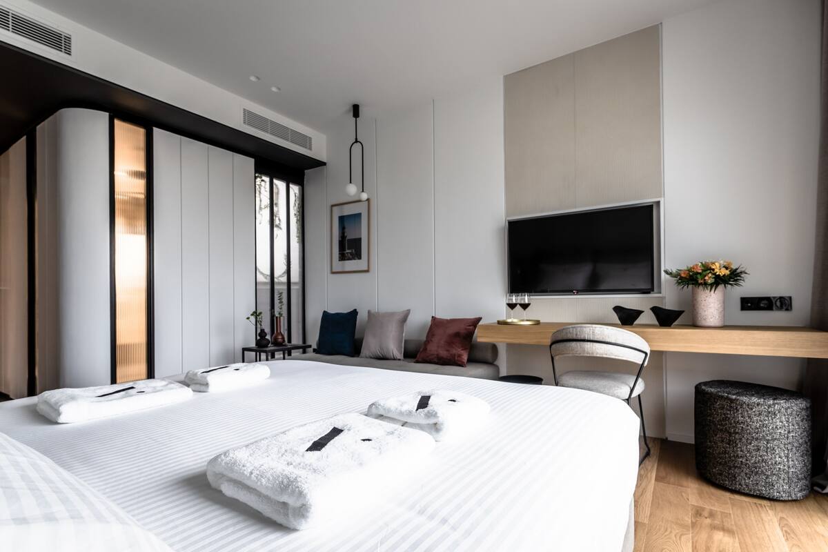 Una habitación de hotel moderna con una cama grande, un escritorio con televisor de pantalla plana, un sofá y una mesita auxiliar.