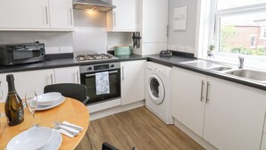 A modern kitchen with white cabinets, a gas stove, a microwave, a washing machine, and a dining area with a table set for two.