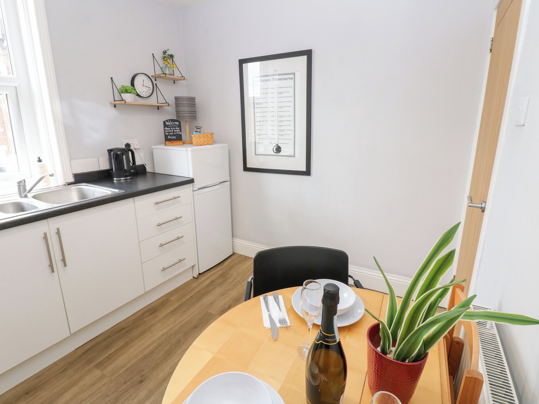A modern kitchen with white cabinets, a black countertop, and a wooden dining table with a bottle of champagne.