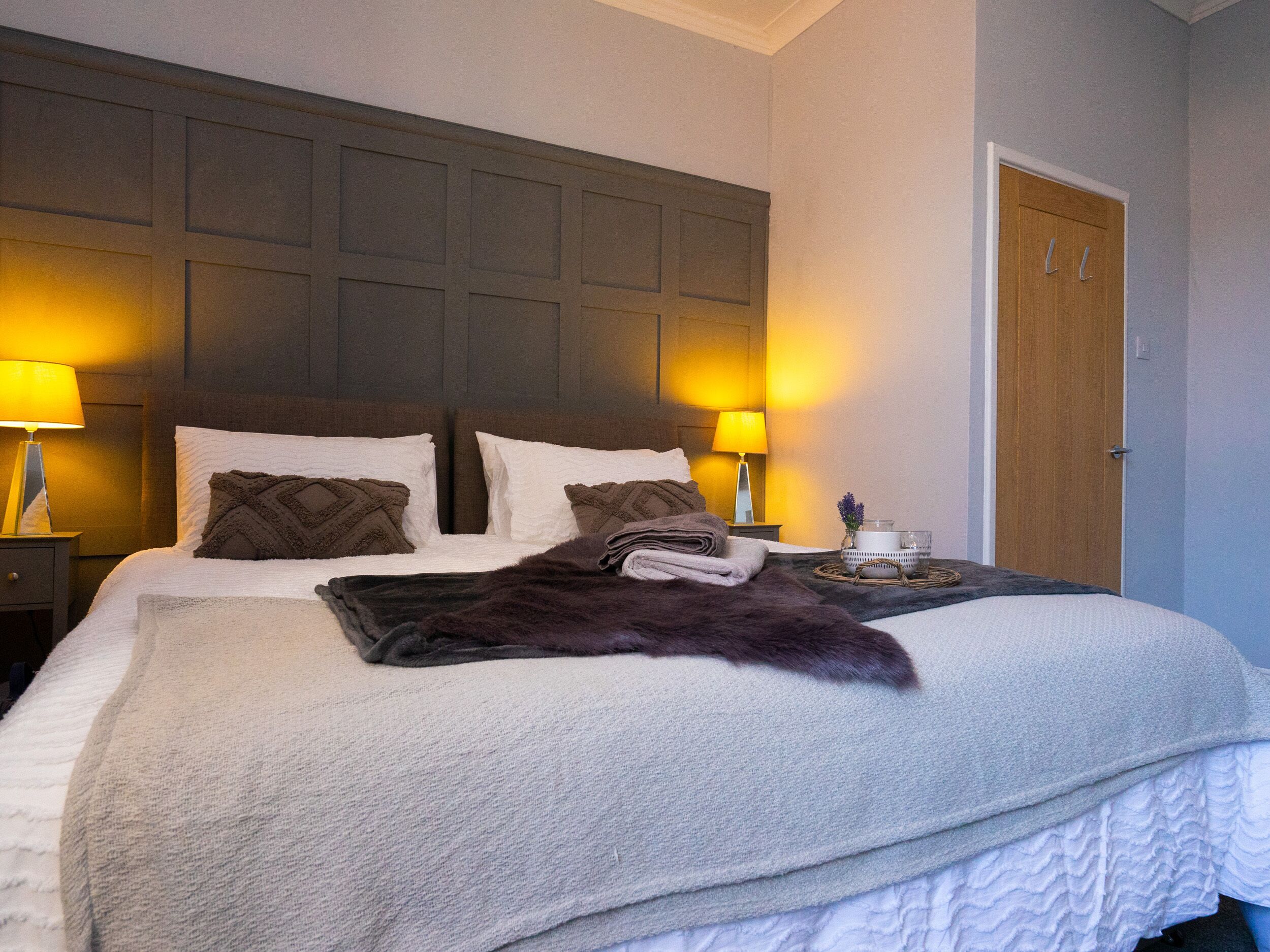 A neatly made bed with a dark throw blanket, two pillows, and a bedside lamp on a nightstand.