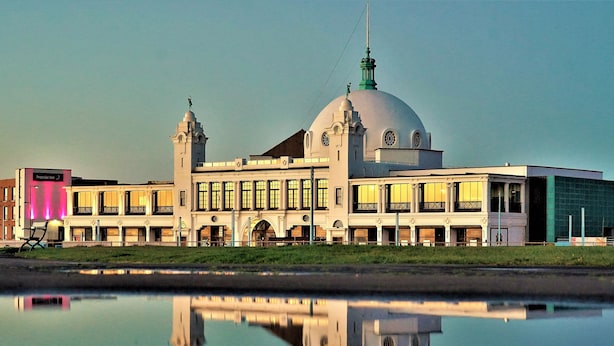 A historic building with a large dome and two towers, reflecting in a calm body of water.