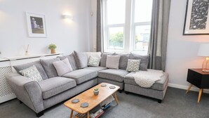A modern living room with a grey sectional sofa, a wooden coffee table, and a black side table with a lamp.