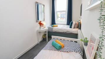 A small, well-lit room with two beds, a bedside table, a mirror, and a window with curtains.