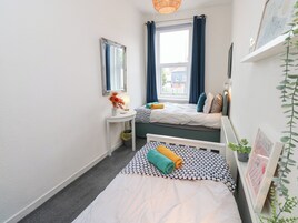 A small, well-lit room with two beds, a bedside table, a mirror, and a window with curtains.