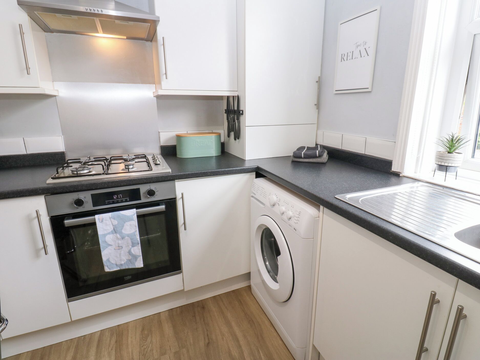 A modern kitchen with white cabinets, a gas stove, an oven, a washing machine, and a sink.