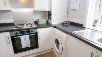 A modern kitchen with white cabinets, a gas stove, an oven, a washing machine, and a sink.