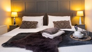 A neatly made bed with two pillows, a fluffy rug, and a bedside table with a lamp.