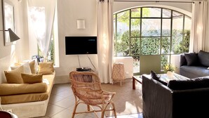 Un salon doté d’une grande fenêtre en arc de cercle, d’un téléviseur à écran plat, d’un canapé, d’un fauteuil et d’une petite table.