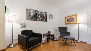 Una sala de estar moderna con un sofá negro, un sillón gris, una mesita con una planta y dos lámparas de pie.