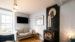 Ein gemütliches Wohnzimmer mit einer Couch, einem kleinen Tisch, einem Kamin und einem an der Wand montierten Fernseher.