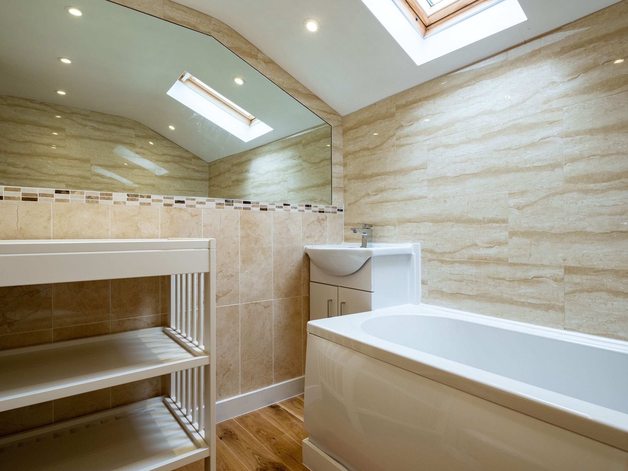 Une salle de bain moderne dotée d’un puits de lumière, d’une baignoire, d’un meuble-lavabo et d’étagères intégrées.