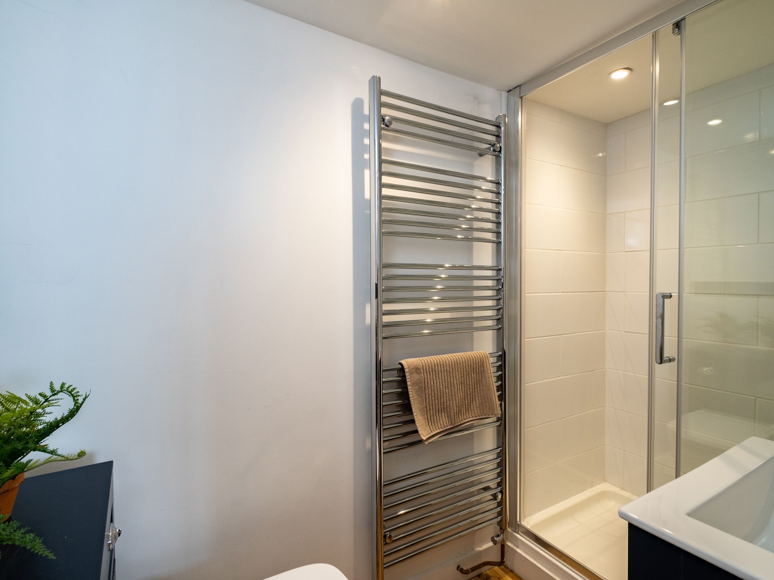 A bathroom with a glass shower enclosure, a towel rack with a towel, and a potted plant.