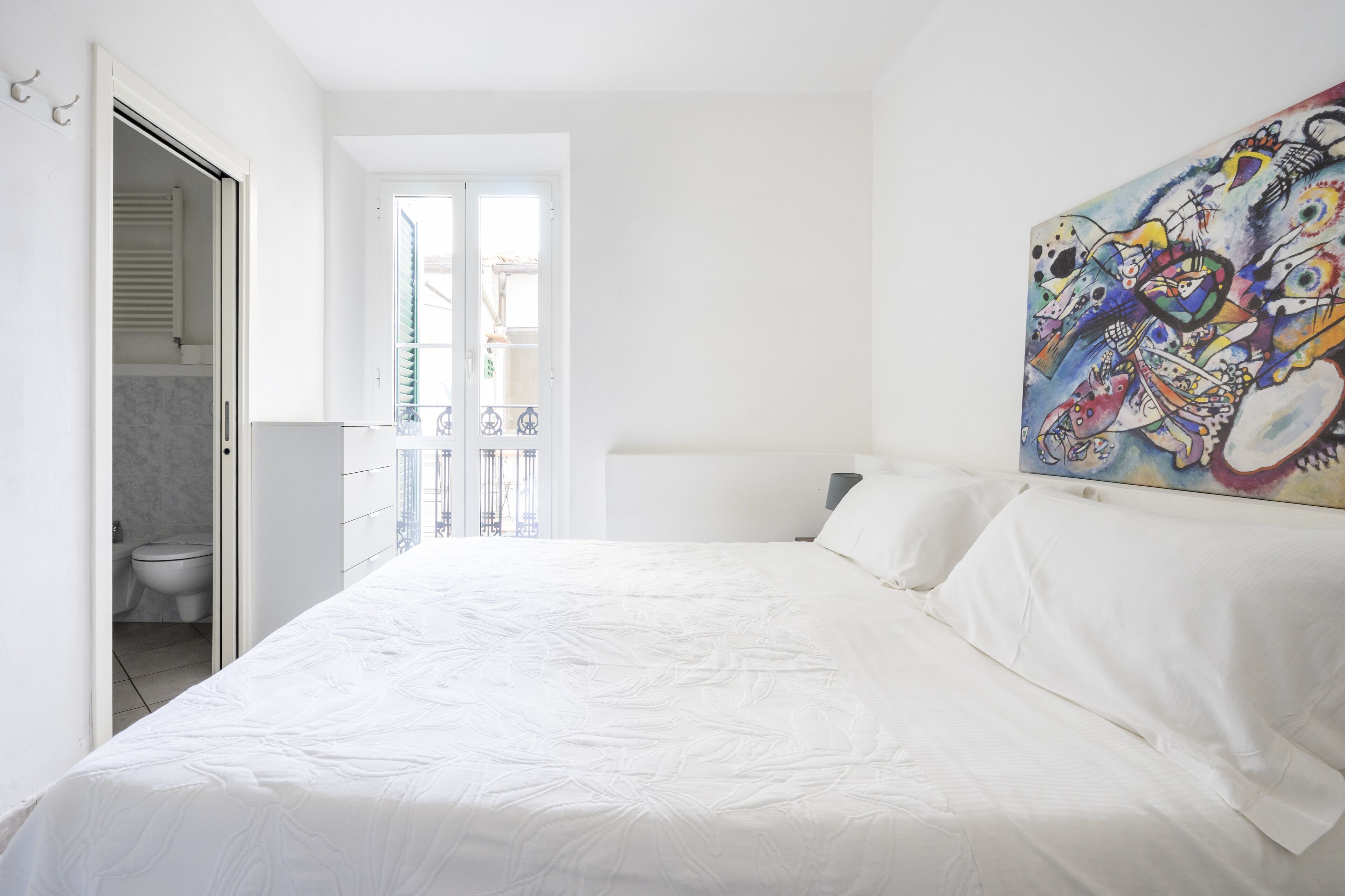 Ein Schlafzimmer mit einem großen Bett, ein Badezimmer mit Toilette und ein Balkon mit Geländer.