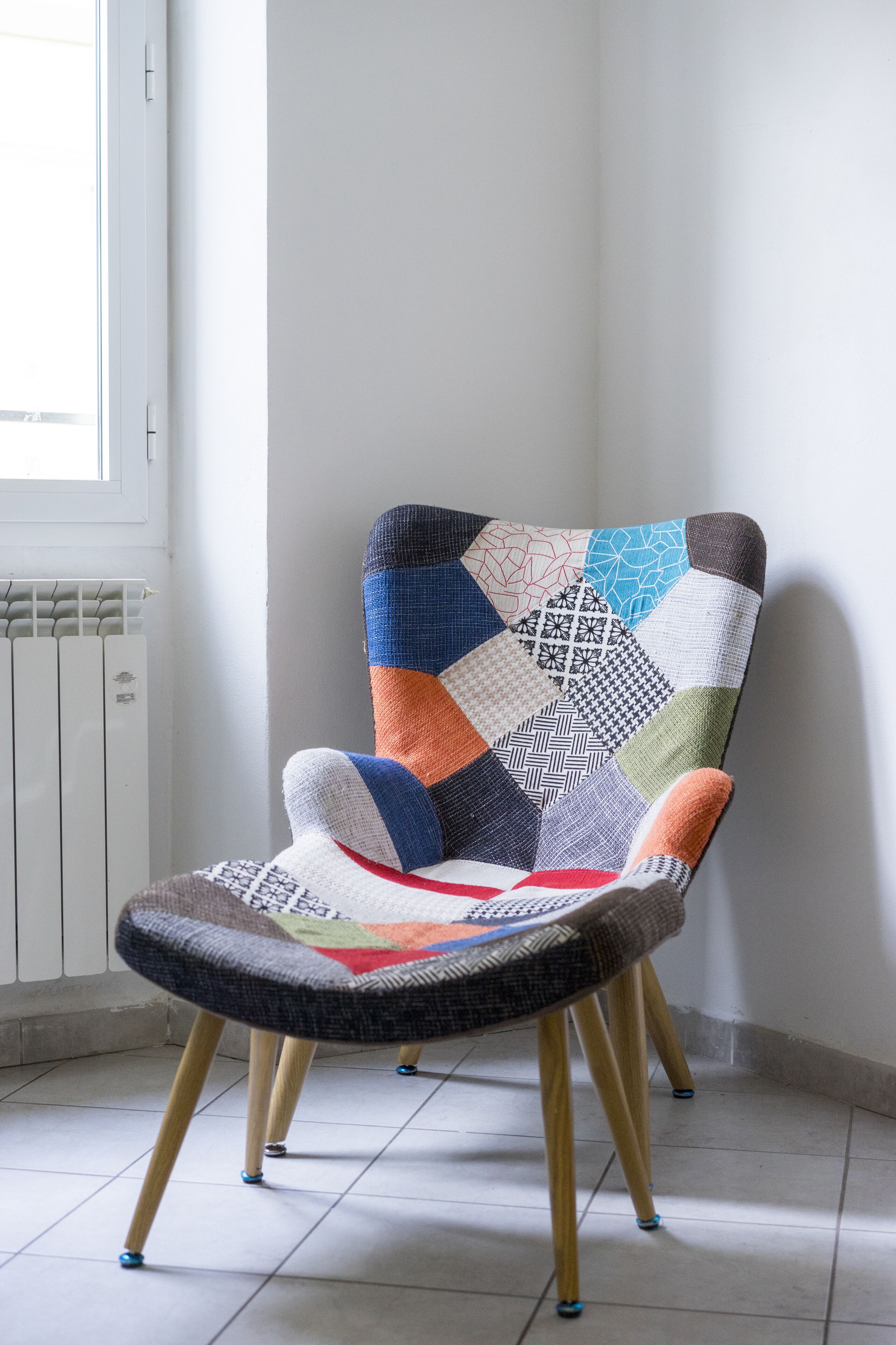 Une chaise au motif patchwork, placée contre un mur près d’une fenêtre et d’un radiateur.